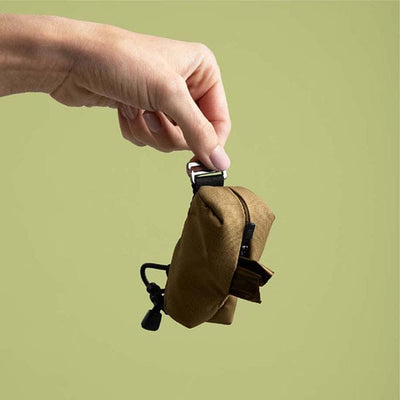 Hand holding a small brown pouch with a green background
