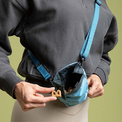 Person holding a blue crossbody bag with a small object in their hand against a green background